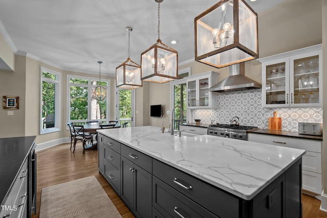 kitchen with wall chimney exhaust hood, sink, a notable chandelier, a center island with sink, and stainless steel range