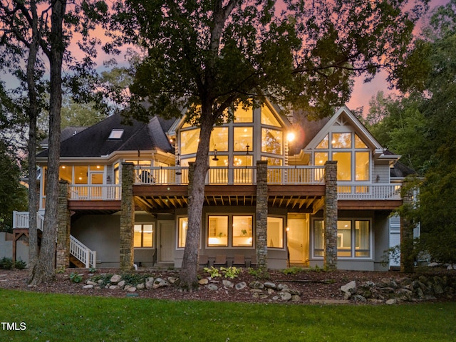 back house at dusk with a lawn and a deck