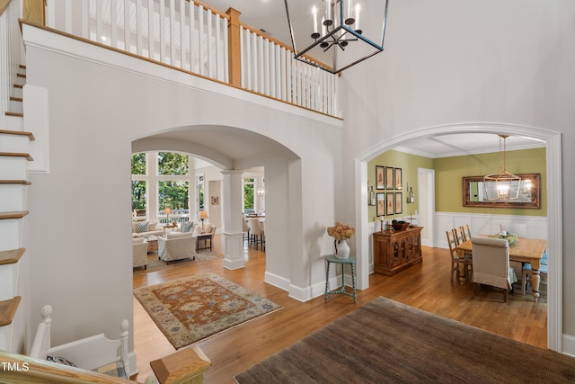 entryway with wood-type flooring, ornamental molding, decorative columns, and a high ceiling