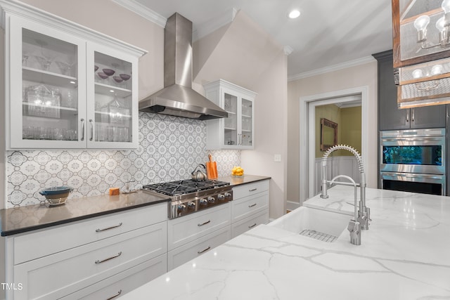 kitchen with wall chimney exhaust hood, tasteful backsplash, sink, stainless steel appliances, and white cabinetry