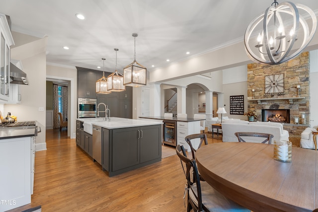 kitchen featuring decorative light fixtures, a center island with sink, decorative columns, and gray cabinetry