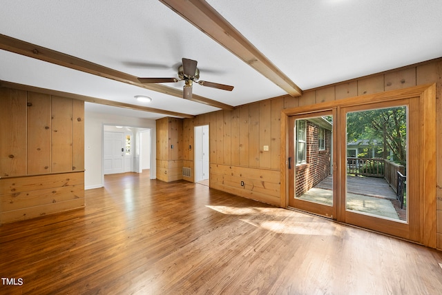 spare room with a textured ceiling, beam ceiling, ceiling fan, hardwood / wood-style flooring, and wooden walls