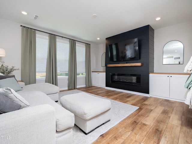 living room featuring light wood finished floors, a fireplace, visible vents, and recessed lighting