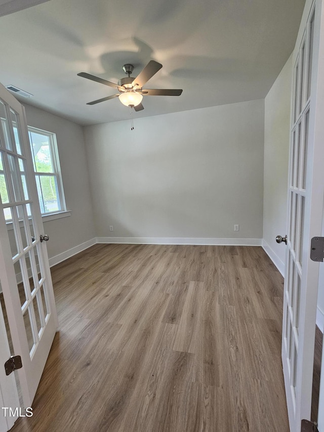 unfurnished room with wood finished floors, a ceiling fan, baseboards, and french doors