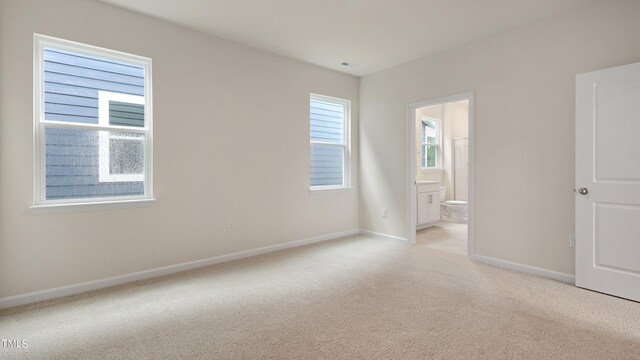 unfurnished bedroom featuring visible vents, ensuite bath, baseboards, and light colored carpet