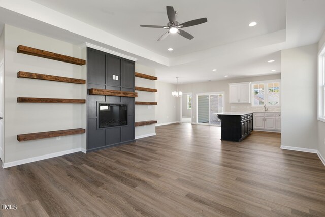 unfurnished living room with ceiling fan with notable chandelier, dark wood-type flooring, and a fireplace