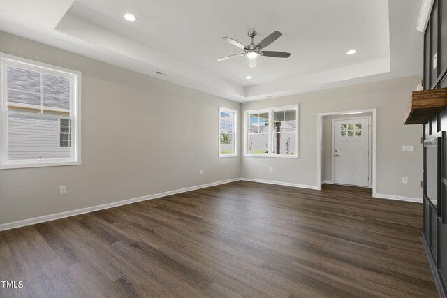 unfurnished living room featuring a tray ceiling, dark hardwood / wood-style flooring, and ceiling fan