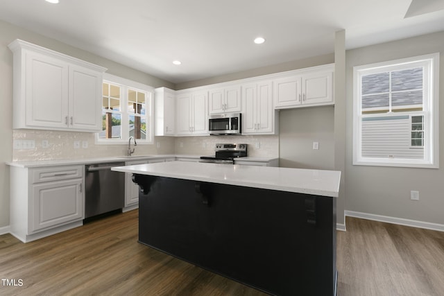 kitchen with sink, a kitchen island, wood-type flooring, white cabinetry, and stainless steel appliances