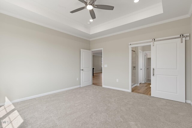 unfurnished bedroom featuring ceiling fan, ornamental molding, a tray ceiling, light colored carpet, and a barn door