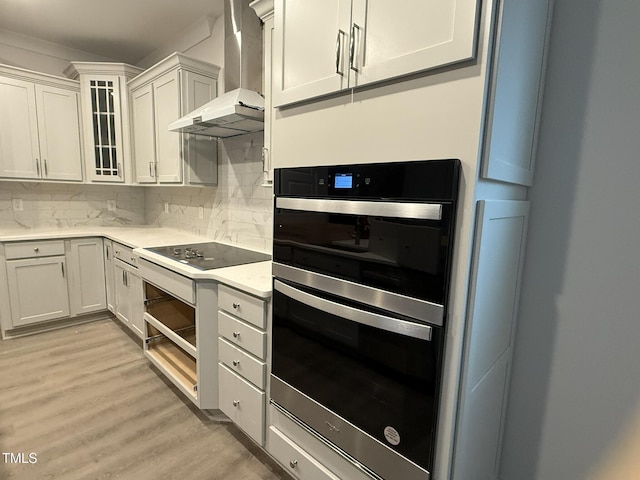 kitchen with double oven, white cabinets, decorative backsplash, light hardwood / wood-style floors, and wall chimney exhaust hood