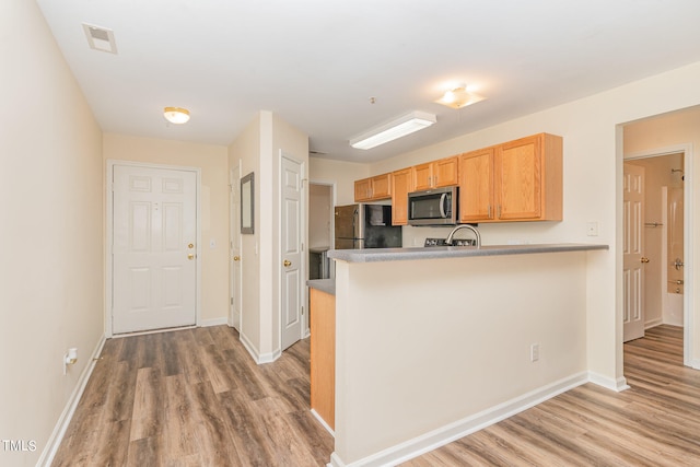 kitchen with light wood-type flooring, kitchen peninsula, light brown cabinets, and stainless steel appliances