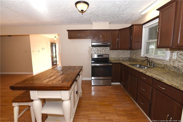 kitchen with dark stone countertops, stainless steel electric stove, light wood-type flooring, a textured ceiling, and sink