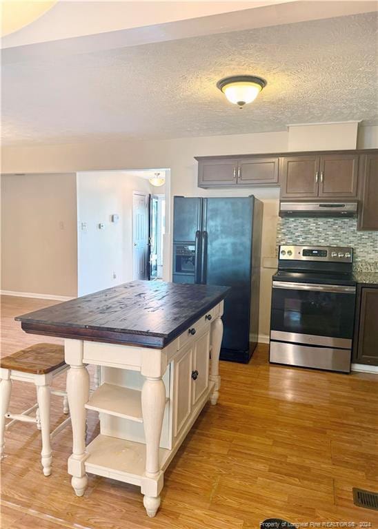 kitchen featuring light wood-type flooring, a textured ceiling, black fridge, backsplash, and stainless steel electric range