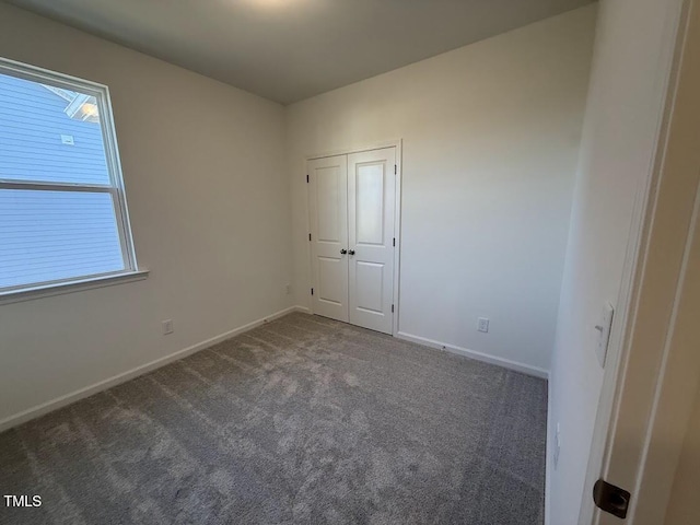 unfurnished bedroom featuring dark colored carpet, a closet, and baseboards