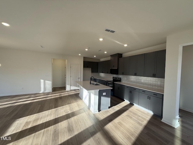 kitchen with a kitchen island with sink, electric range, a sink, open floor plan, and light countertops