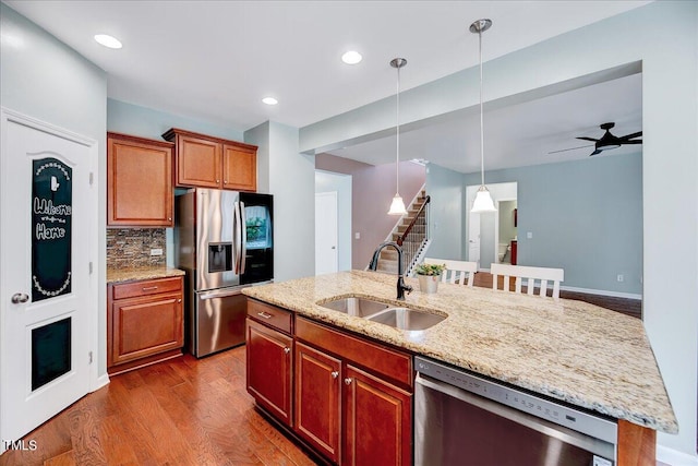 kitchen with sink, a center island with sink, dark wood-type flooring, appliances with stainless steel finishes, and decorative backsplash