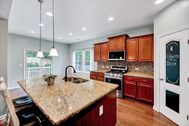 kitchen featuring light wood-type flooring, sink, a kitchen island with sink, stainless steel appliances, and light stone countertops