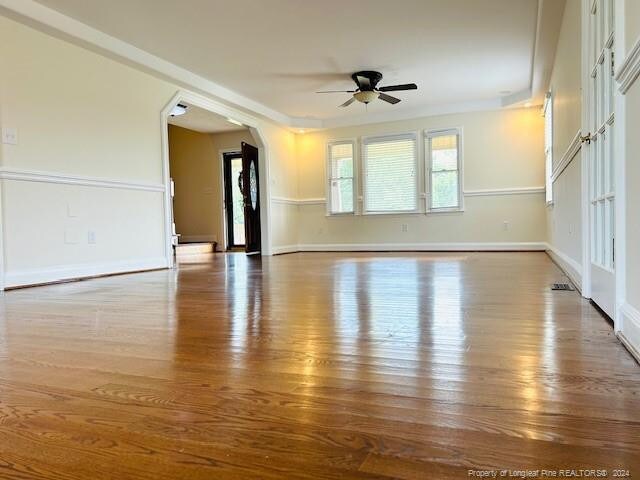unfurnished living room with ceiling fan, wood finished floors, baseboards, and arched walkways