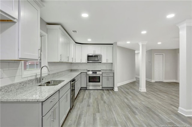 kitchen featuring sink, stainless steel appliances, light stone countertops, light hardwood / wood-style floors, and backsplash