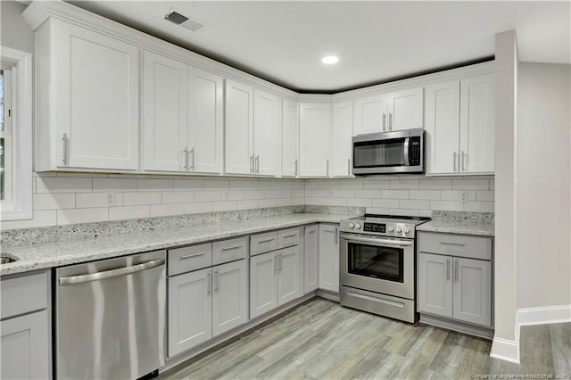 kitchen with light wood-type flooring, appliances with stainless steel finishes, white cabinets, light stone countertops, and backsplash