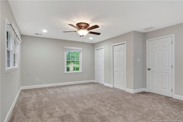 unfurnished bedroom featuring light carpet, two closets, and ceiling fan