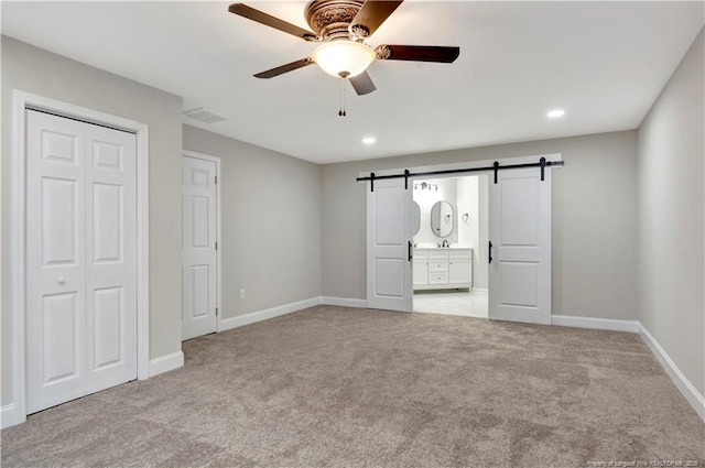 unfurnished bedroom with connected bathroom, light colored carpet, ceiling fan, a barn door, and a closet