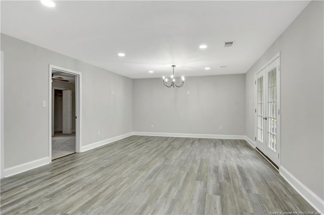 unfurnished room with an inviting chandelier, wood finished floors, visible vents, and baseboards