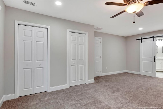 unfurnished bedroom featuring a barn door, visible vents, baseboards, carpet, and two closets