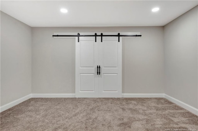 unfurnished room featuring a barn door, recessed lighting, carpet flooring, and baseboards