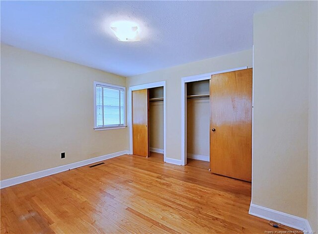 unfurnished bedroom with light hardwood / wood-style flooring and two closets