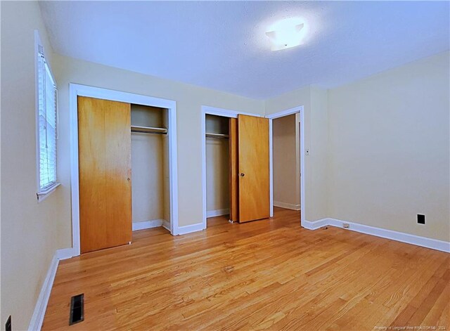 unfurnished bedroom with light wood-type flooring and multiple closets