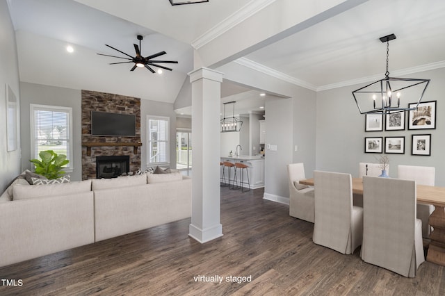 dining space with a healthy amount of sunlight, a stone fireplace, ceiling fan with notable chandelier, and dark hardwood / wood-style floors