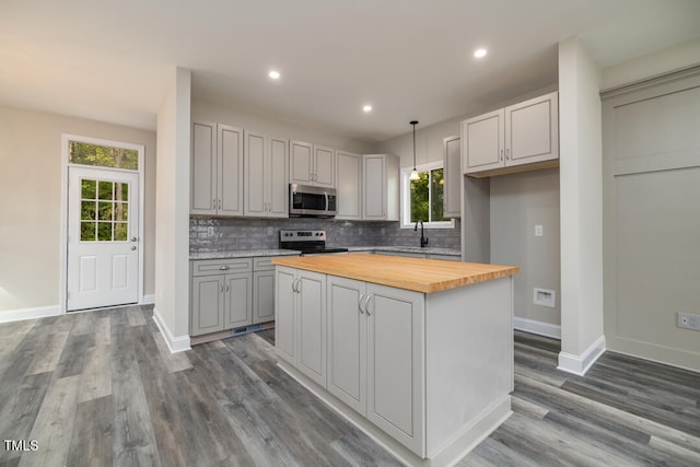 kitchen with pendant lighting, stainless steel appliances, a center island, hardwood / wood-style floors, and wood counters