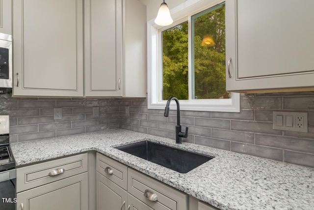 kitchen featuring appliances with stainless steel finishes, decorative backsplash, light stone countertops, decorative light fixtures, and sink