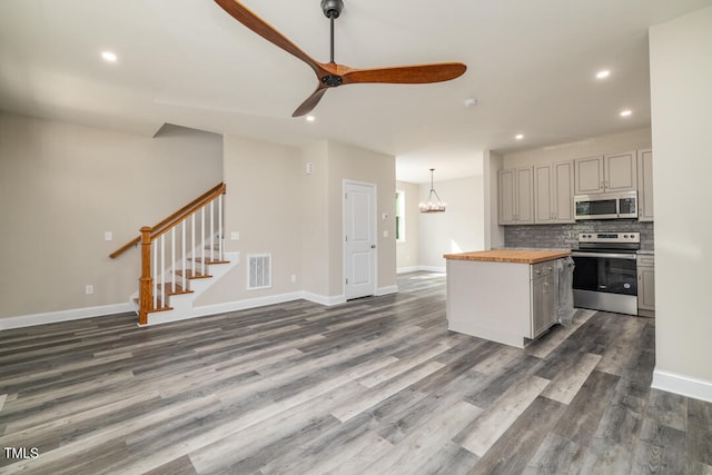 kitchen with decorative backsplash, dark wood-type flooring, ceiling fan with notable chandelier, butcher block counters, and stainless steel appliances