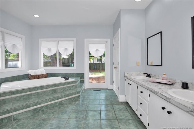 bathroom with tiled tub, vanity, tile patterned flooring, and a wealth of natural light