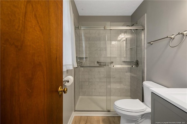 bathroom with vanity, toilet, hardwood / wood-style floors, and a shower with door