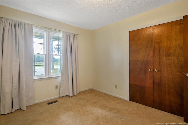 unfurnished bedroom featuring a textured ceiling, light colored carpet, and a closet