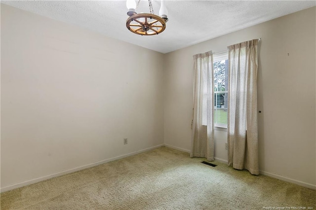 spare room with a textured ceiling, light carpet, and a notable chandelier