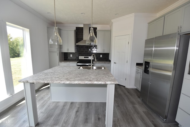 kitchen featuring a kitchen island with sink, wall chimney range hood, hanging light fixtures, sink, and appliances with stainless steel finishes