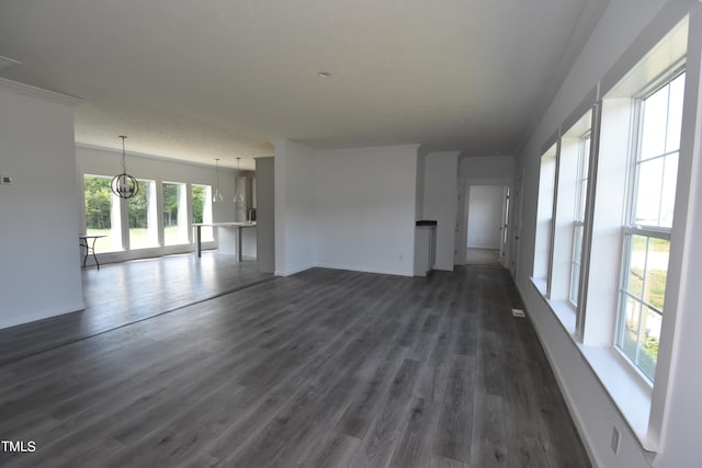 unfurnished living room featuring an inviting chandelier, dark wood-type flooring, and crown molding