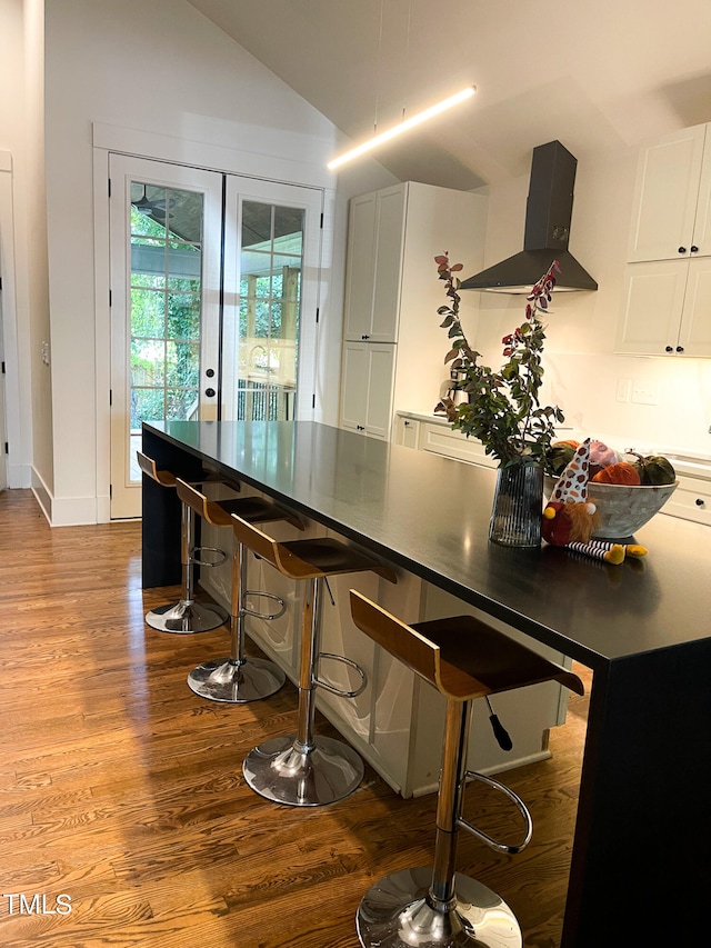 kitchen with white cabinetry, a breakfast bar area, ventilation hood, light wood-type flooring, and lofted ceiling