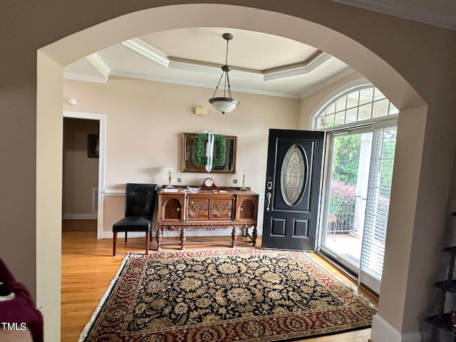 entryway with ornamental molding, light wood-type flooring, and a tray ceiling