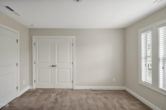 unfurnished bedroom featuring multiple windows, a closet, and light carpet