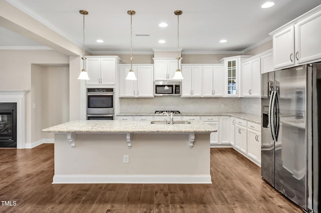 kitchen with appliances with stainless steel finishes, white cabinetry, hanging light fixtures, light stone countertops, and a center island with sink