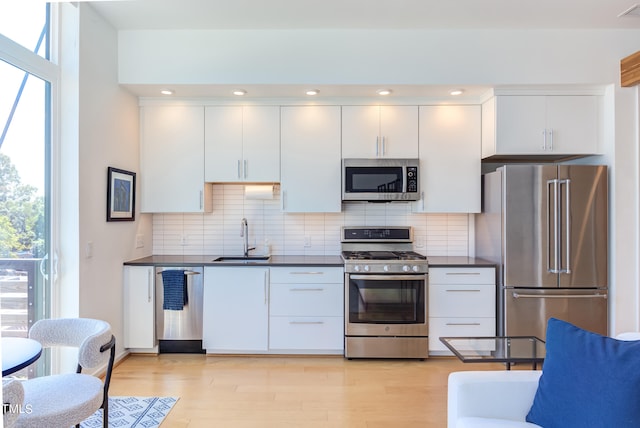 kitchen with white cabinets, sink, light hardwood / wood-style flooring, backsplash, and appliances with stainless steel finishes