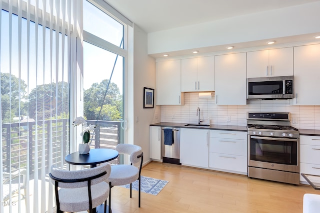 kitchen featuring white cabinets, sink, backsplash, appliances with stainless steel finishes, and light hardwood / wood-style floors