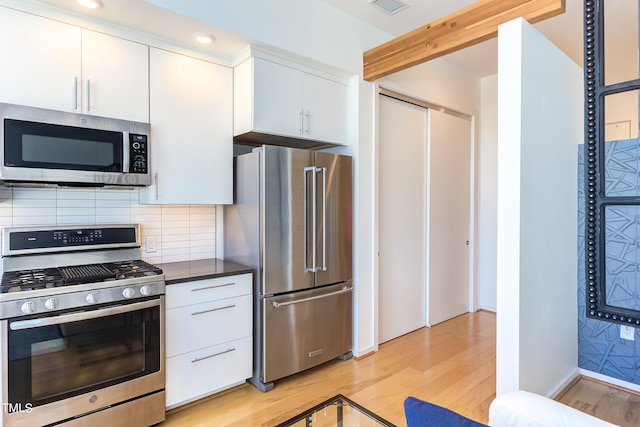 kitchen featuring appliances with stainless steel finishes, light wood-type flooring, white cabinetry, and decorative backsplash