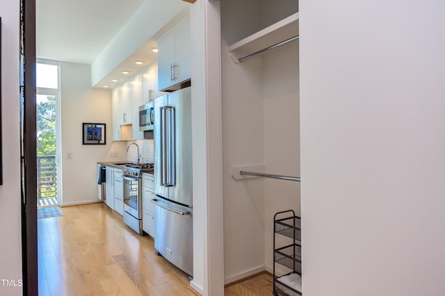 kitchen with decorative backsplash, white cabinets, stainless steel appliances, light hardwood / wood-style flooring, and sink