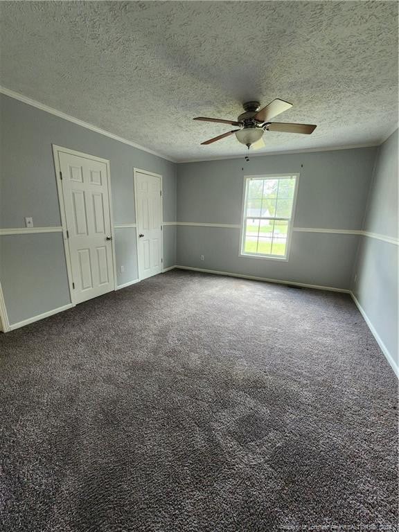 empty room with carpet floors, a textured ceiling, ornamental molding, and ceiling fan